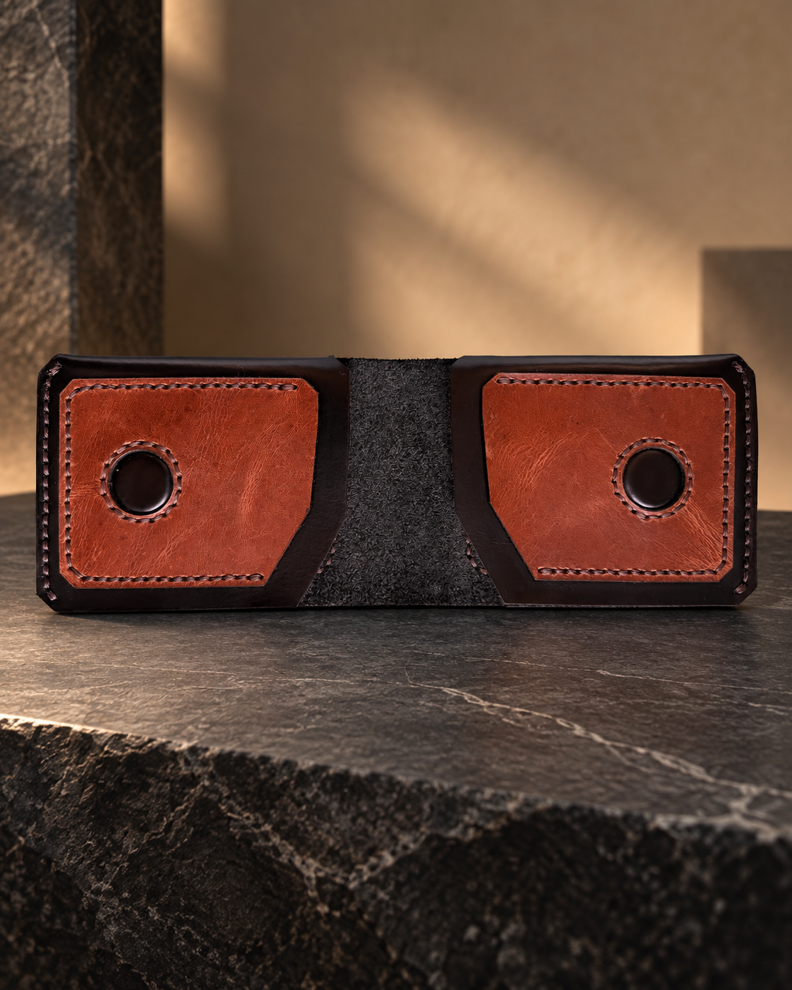 Premium handcrafted leather wallet in black and brown, featuring a dual-panel design, detailed stitching, and a textured center, displayed on a warm walnut wood surface.