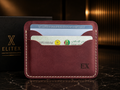 A burgundy leather card holder wallet with white contrast stitching, featuring an embossed 'EX' logo on the bottom right. It is shown holding two cards, positioned in front of a black EliteX branded box on a dark marble surface.