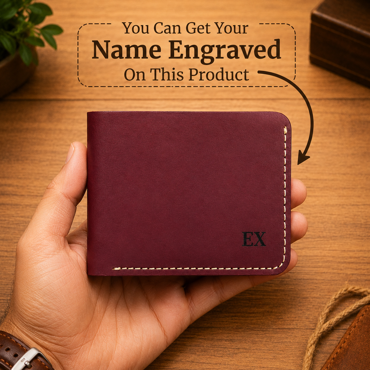A hand holds a burgundy leather wallet with white contrast stitching and an engraved 'EX' on the front, set against a wooden desk background with promotional text about custom name engraving.